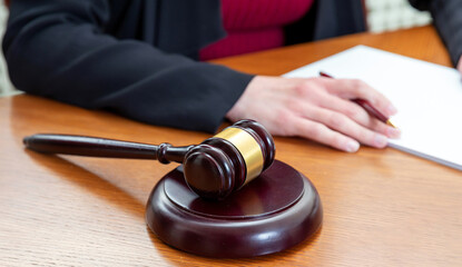 Law courtroom, Judge Bench. Woman sitting, auction gavel and notepad on wooden table, close up.