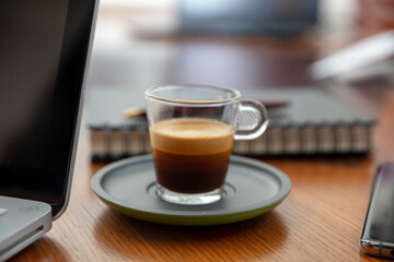 Espresso coffee cupon a wooden desk close up. Computer laptop and business office background