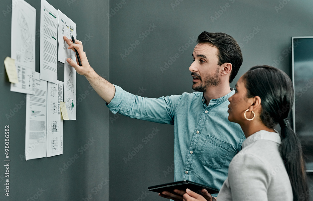 Poster Success is designed through the efforts of a team. Shot of two architects working with blueprints on a wall in an office.