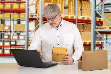 Warehouse business owner. Man with box in his hands in front of laptop. Male business owner with computer. Concert owner of online store. Preparing online orders for shipment. Warehouse manager