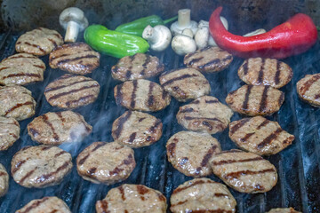 Grilled meatballs,tomatos ,peppers and mushrooms shown on a grill while cooking with somoke on them