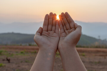 Human hands praying to god on mountain sunset background