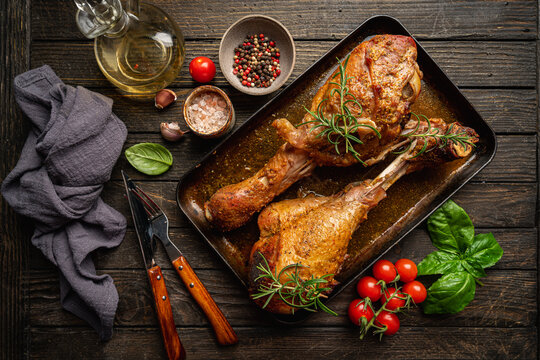 baked fried turkey thighs, rubbed with spices and salt on a baking sheet with garlic and rosemary on dark background, top view