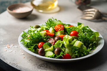 Classic vegetable salad with fresh olives, tomatoes, cucumbers and olive oil on gray background.
