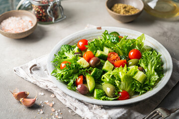 Classic vegetable salad with fresh olives, tomatoes, cucumbers and olive oil on gray background.
