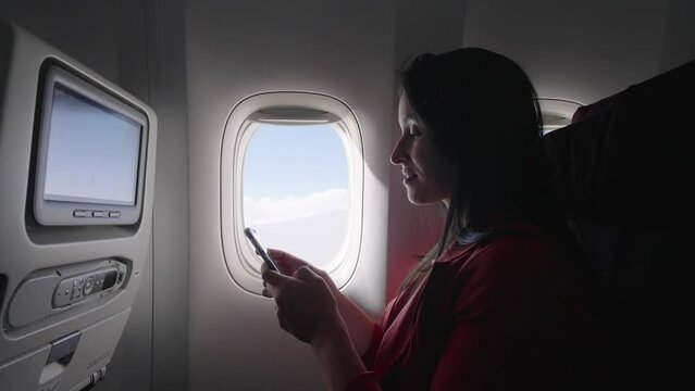 Caucasian female passenger chatting online via cellphone using wifi internet connection on board. Young woman browsing network during flight
