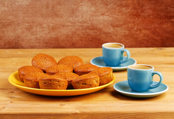 Freshly baked homemade cupcakes and two cups of coffee espresso on wooden table.