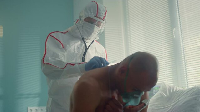 Doctor examine covid19 patient back with stethoscope in protective suit mask. 