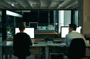 Making success happen at all hours of the day and night. Rearview shot of two businesspeople working on computers in an office at night.