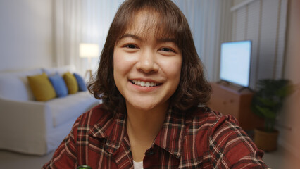 Fototapeta premium Selfie view of young happy attractive asia woman enjoy relax night party event online celebration festive with friends at home clinking beer cheers with bottle toasting drinking via online video call.