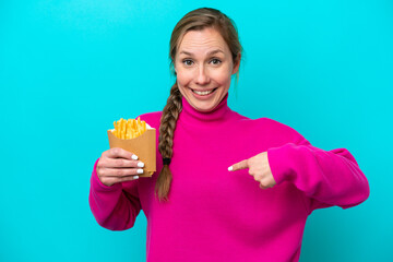 Young caucasian woman holding fried chips isolated on blue background with surprise facial expression