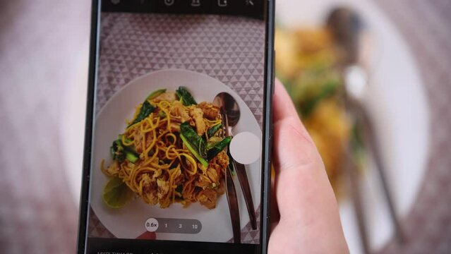 Taking picture of plate with fried yellow noodle with smartphone. Close up