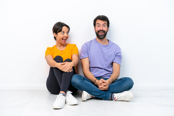 Fototapeta na wymiar Young caucasian couple sitting on the floor isolated on white background with surprise facial expression