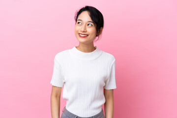 Young Vietnamese woman isolated on pink background looking up while smiling