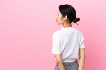 Young Vietnamese woman isolated on pink background in back position and looking back