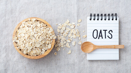 Rolled oat in wooden bowl with spoon and oats word on notebook