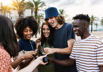 Group of young friends enjoying summertime together - United multiracial people laughing on party while drinking beers at summer vacation - Focus on african man