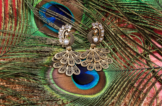 "Closeup of pair of beautiful peacock shaped earrings on colorful background"