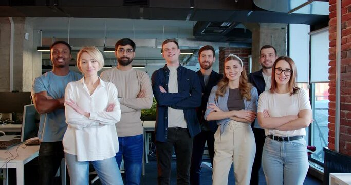 Portrait shot of mixed-races people standing in office, smiling to camera and crossing hands in front of them. Multiethnic men and women. Young group of IT startup.