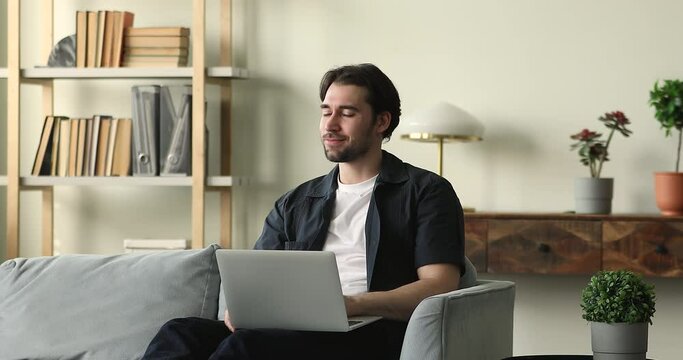 Pensive young man author sit on sofa create story text using laptop smile on funny idea hilarious plot device. Inspired millennial male screen writer work on scenario to new film movie play tv show