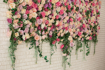 Beautiful decorative colorful roses and peonies on brick white wall. Interior wedding party decor. Wall with curly Flowers. Brick wall with beautiful flowers in room. Summer flowers on wall building.	