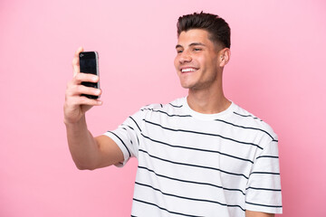 Young caucasian man isolated on pink background making a selfie