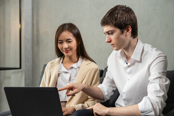 Young caucasian businessman and businesswoman work together, look at computer, man point to laptop, selective focus at man. Young man and woman work business in home office and copy space background