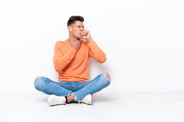 Young man sitting on the floor isolated on white background is suffering with cough and feeling bad