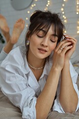 Fototapeta premium A woman in a white shirt lies on her stomach in bed. Portrait of an attractive girl on the bed.
