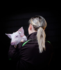 Schweinehaltung - tierliebe, attraktive Frau mit einem Ferkel vor schwarzem Hintergrund.