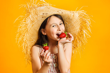 Little happy girl eat red ripe strawberries. Sweet juicy summer fruits. Yellow wall background in...