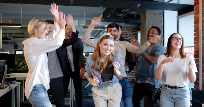 Mixed-races men and women celebrating end of working week in office. Multiethnic coworkers dancing and having fun ar workplace. Young team of company employees having party.
