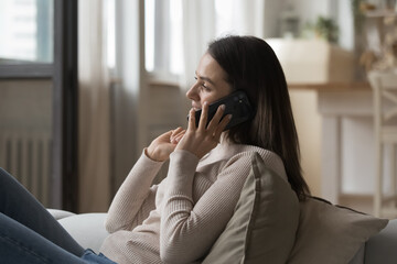 Fototapeta na wymiar Happy millennial cell user woman speaking on mobile phone, enjoying telephone talk, making call, laughing, smiling, listening to good news, relaxing on couch at home. Communication concept