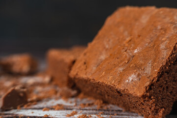 Chocolate brownies on a rustic wooden table with chocolate chips and chocolate soil next to the brownie portions.Close up.