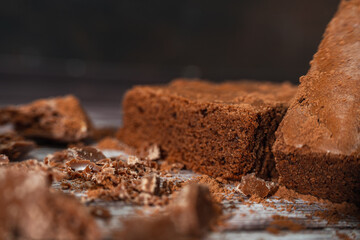 Chocolate brownies on a rustic wooden table with chocolate chips and chocolate soil next to the brownie portions.Close up.