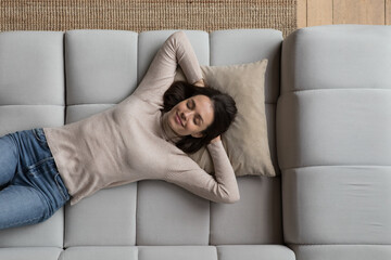 Happy relaxed pretty young woman lying on sofa at home, daydreaming, thinking over good future plans, breathing fresh air, enjoying leisure time, pause, laziness, reloading. Top view