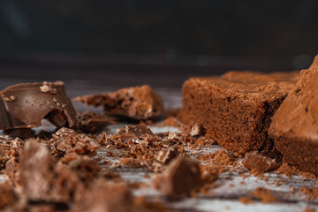 Chocolate brownies on a rustic wooden table with chocolate chips and chocolate soil next to the brownie portions.Close up.