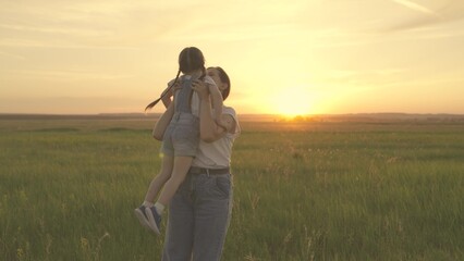Mom hugs her kid daughter, picks her up and curls up in park at sunset. Little girl, kid hugs mom in park in spring. Kid smiles, plays with his mother. Happy childhood, family, mother loves daughter