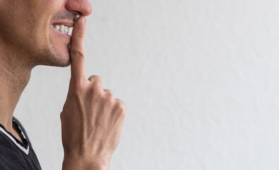 Keep it in secret. Young unshaven man in white tshirt showing silence gesture, making shh and...