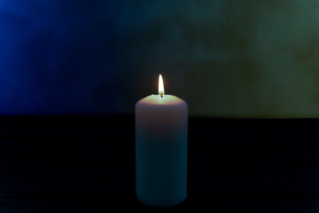 Biała świeca płonąca na ciemnym tle posiadającym delikatne niebieski i żółte zabarwienie. Hołd i wyraz solidarności z ofiarami wojny w Ukrainie. - 498106597