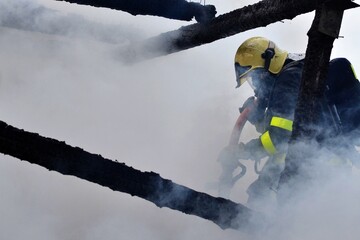 A firefighter with a breathing apparatus and a hose in the smoke extinguishes a warehouse fire
