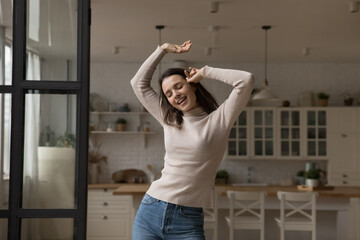 Carefree cheerful millennial dancer girl having fun at home, singing songs with closed eyes, dancing to music alone in apartment interior, moving body, enjoying energetic activity, exercises