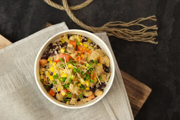 Healthy bowl with wild rice, chicken and vegetables on wooden board on dark background. Food delivery service and daily ration concept.