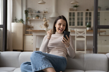 Joyful happy smartphone user woman excited with good news, looking at text message on cellphone screen, reading notice, making winner achieve yes hand, laughing, feeling joy. Communication concept