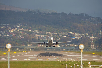 White passenger plane fly up over take-off runway from airport, against the backdrop of hills and...