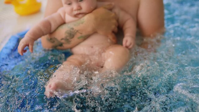 Cute baby having swimming lesson with his mother and father. Healthy family teaching their baby to swim in the swimming pool. Young father takes his son and embraces him while the kid is smiling