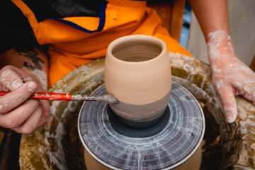 Potter working on potters wheel with clay. Process of making ceramic tableware in pottery workshop. Handicraft and art concept.