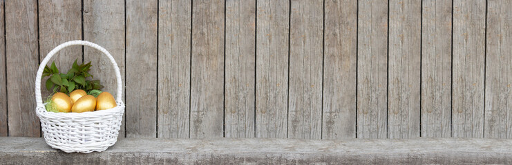 Easter banner, golden eggs in a white basket. Wooden background with copy space