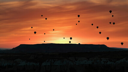 Silhouettes of hot air balloons flying in Cappadocia landscape with dramatic morning sky, Turkey