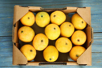 fresh ripe yellow mango fruit in corrugated box isolated on wood background
